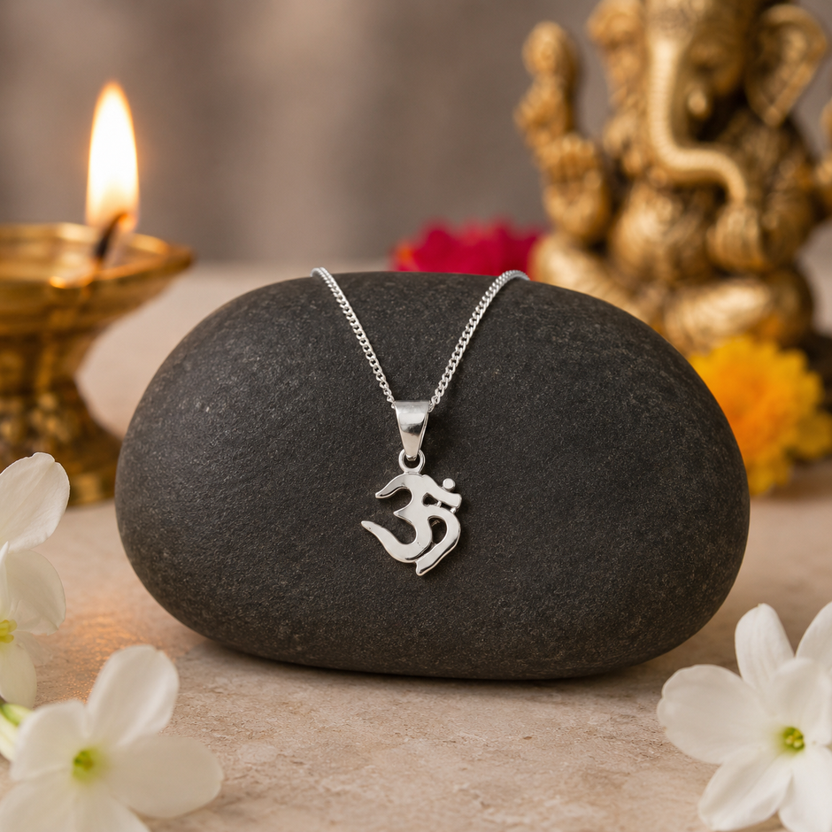 Om pendant in brass with silver finish resting on dark stone surrounded by white jasmine flowers and diya
