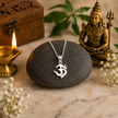 Om pendant brass silver finish on black stone with Lord Shiva idol and diya in background