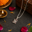 Tirupati Balaji pendant with red enamel detail on dark surface with diya, rose petals and wooden box in background