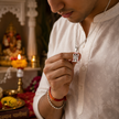 Tirupati Balaji pendant with red enamel in brass silver finish held by man in white kurta while praying in front of temple setup