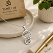 Tamil Om pendant in brass silver finish worn on silver chain displayed on marble plate with diya and Om Namah Shivaya frame in background
