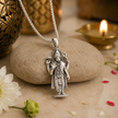 Lord Vishnu Ji pendant in brass silver finish resting on pebble stone with white chrysanthemum flower, rose petals and diya in warm devotional setting