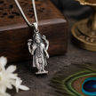 Lord Vishnu Ji pendant in brass silver finish resting against carved wooden block with peacock feather and brass lamp in background