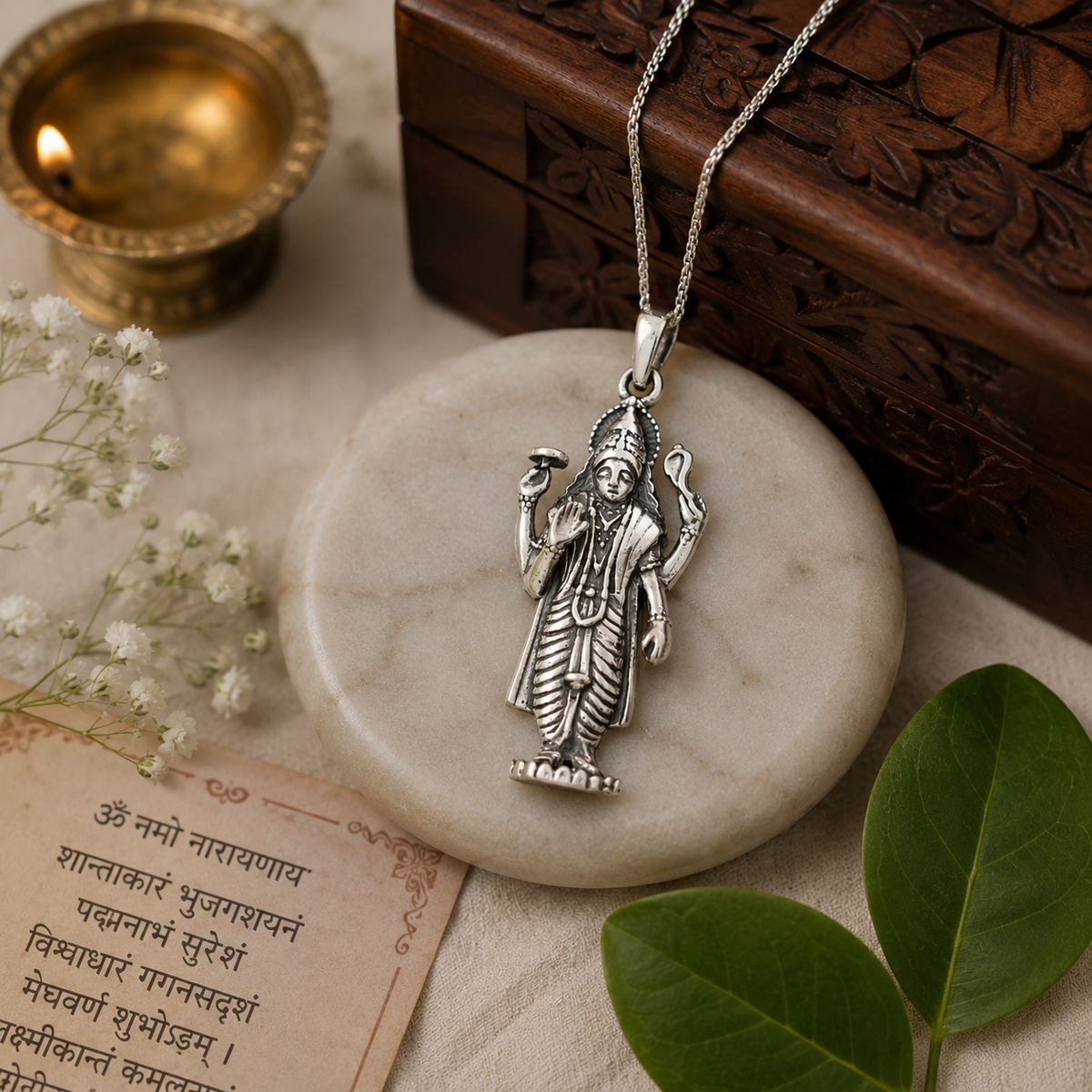Lord Vishnu Ji pendant in brass silver finish on white marble disc with Om Namo Narayanaya scripture, diya, green leaves and wooden box in background