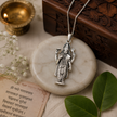 Lord Vishnu Ji pendant in brass silver finish on white marble disc with Om Namo Narayanaya scripture, diya, green leaves and wooden box in background