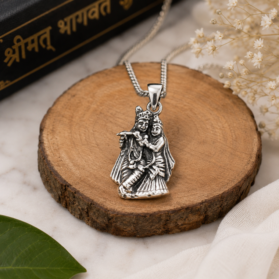Radha Krishna pendant in brass silver finish on wooden slice with silver chain, Shrimad Bhagavat scripture in background and baby’s breath white flowers