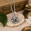 Shiv Parvati Ji pendant in brass silver finish on white pebble stone with silver chain, Shiv Purana book in background, green bael leaf, jasmine flower and lit brass diya