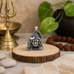 Mahadev Ji Shiv Ji face pendant in brass silver finish on wooden slice with brass trishul lamp, rudraksha bracelet, white pebbles and green leaves in background