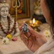 Woman in white holding Mahadev Ji brass silver pendant in both hands in front of white Shiva marble idol with rudraksha mala, lit diya, lotus and white flowers at home temple