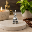 Gautam Buddha meditating pendant in brass antique silver finish on concrete disc with rudraksha mala, lit candle, gold Buddha idol and green plant in calm mindful setting