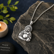 Laughing Buddha pendant in brass antique silver finish on dark grey rock with silver chain, lit candle, green leaves and Peace Happiness Positivity inscription on stone