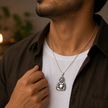 Man in white t-shirt and dark jacket wearing Laughing Buddha brass antique silver pendant on silver chain with warm candlelight in background showing pendant for daily wear