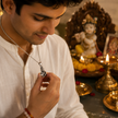 Man in white kurta wearing Laddu Gopal Baby Krishna brass antique silver pendant on silver chain holding pendant gently while looking at it with devotion in front of Krishna idol brass diyas marigold flowers at home temple