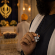 Sikh man holding Khanda Pendant at Gurudwara with golden Khanda and diya in background — symbol of faith and strength