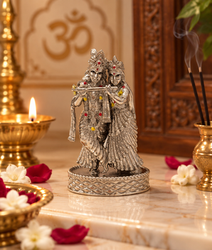 Silver finish Radha Krishna idol with Krishna playing flute, displayed in a traditional home temple with diya, incense and flowers – My Guru Ji.