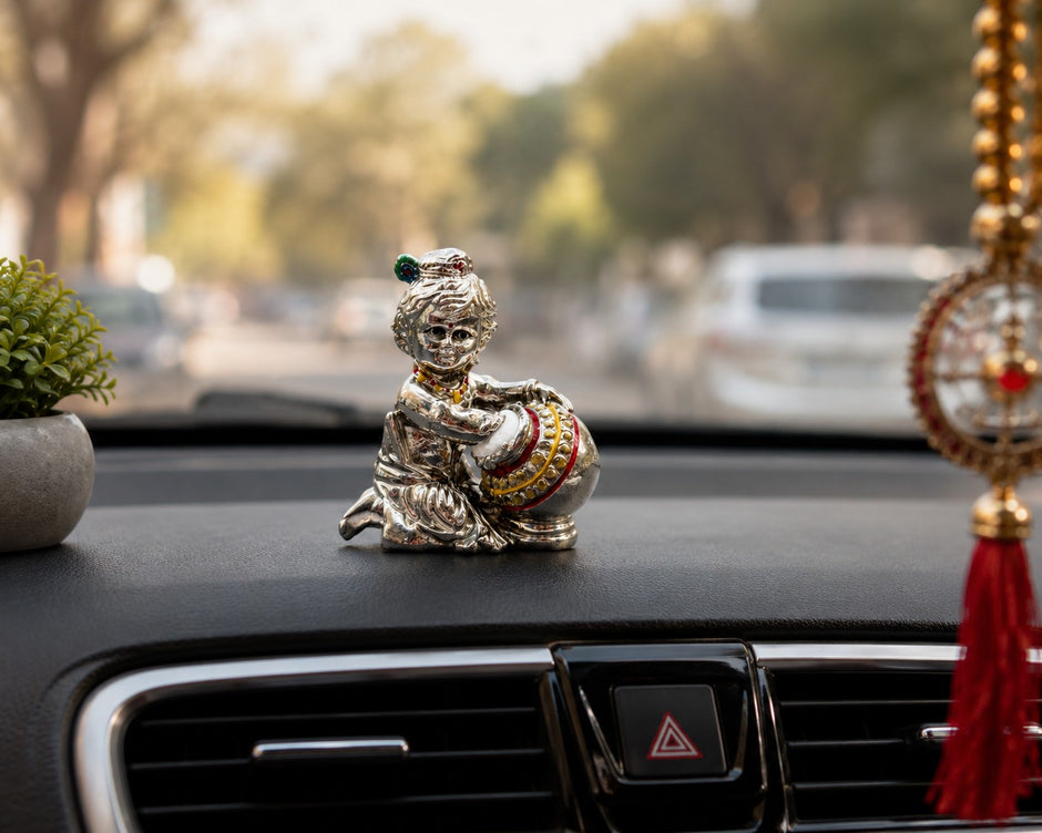 My Guru Ji silver finish brass Laddu Gopal Makhan Chor idol placed on a car dashboard with decorative accents.