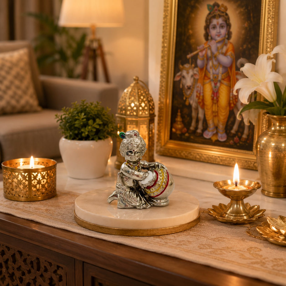My Guru Ji silver finish brass Laddu Gopal Makhan Chor idol placed on a marble stand with candles and decor