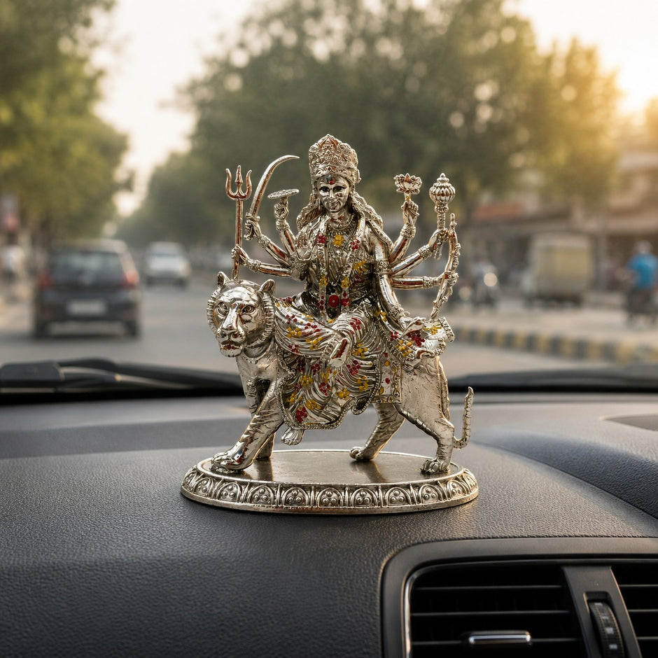 My Guru Ji brass Maa Durga idol with silver finish, seated on a lion, displayed on a car dashboard.