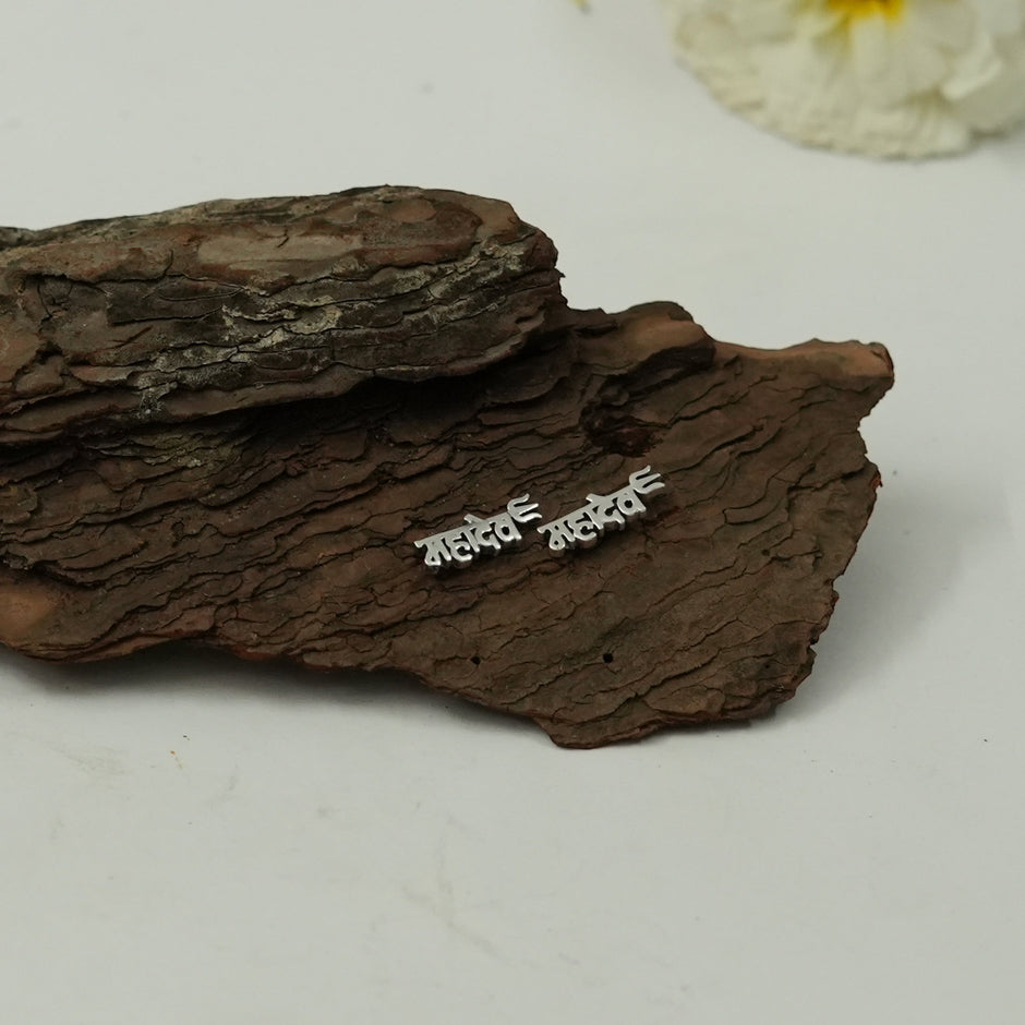My Guru Ji Mahadev stud earrings in polished silver featuring Hindi script on a rustic wooden bark background.