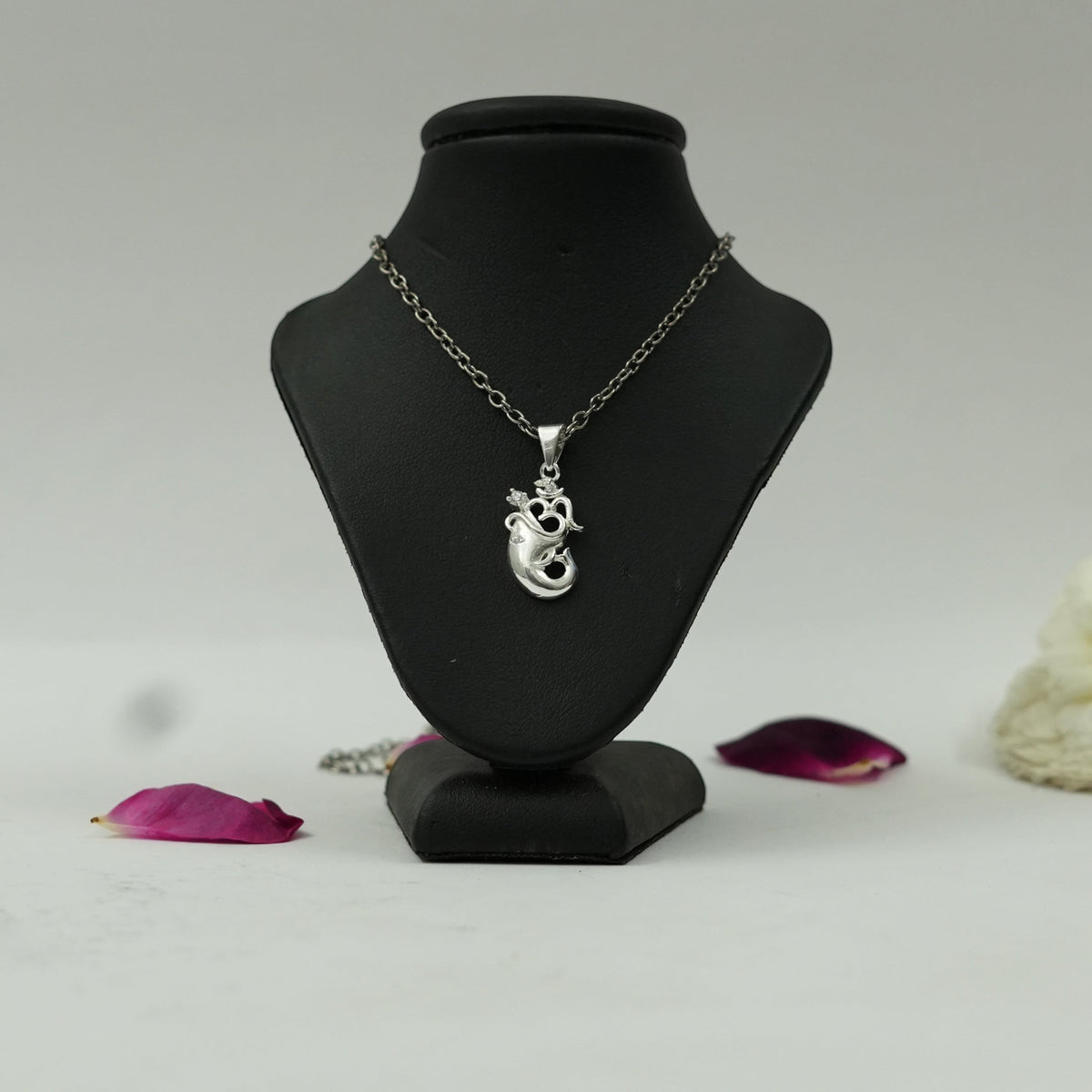 My Guru Ji silver finish Om and Ganesh Ji spiritual pendant on a black display stand with rose petals