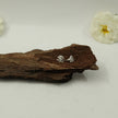 My Guru Ji Om symbol stud earrings in silver finish, crafted from brass, displayed on a piece of natural wood.