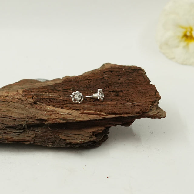 My Guru Ji silver finish brass Om symbol stud earrings resting on a piece of natural wood