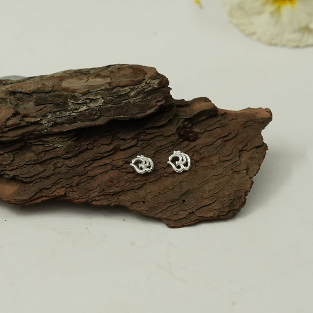 My Guru Ji silver-finished brass Om symbol stud earrings displayed on a piece of natural tree bark