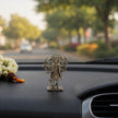My Guru Ji silver finish brass Panchmukhi Hanuman idol standing on a car dashboard with a blurred road background.