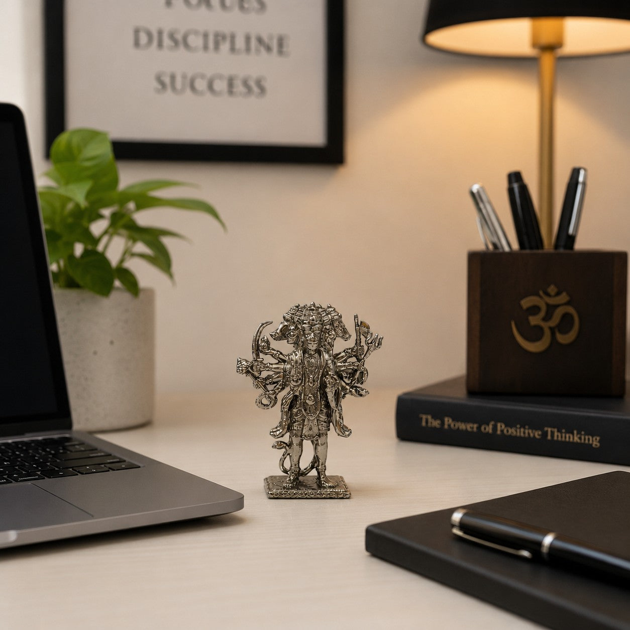 My Guru Ji silver-finished brass Panchmukhi Hanuman idol displayed on an office desk next to a laptop and books.