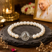 My Guru Ji pearl bracelet with a silver-finish brass charm featuring Guru Ji, set on a dark stone display.
