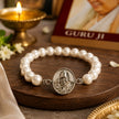 My Guru Ji pearl bracelet featuring a silver-finish brass Guru Ji charm on a wooden surface with a lit diya nearby.