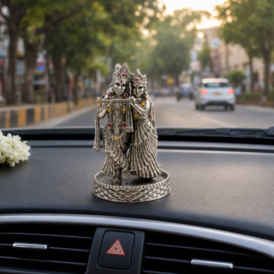 My Guru Ji Radha Krishna idol in silver-finish brass with stone accents, displayed on a car dashboard.