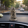 My Guru Ji Radha Krishna idol in silver-finish brass with stone accents, displayed on a car dashboard.