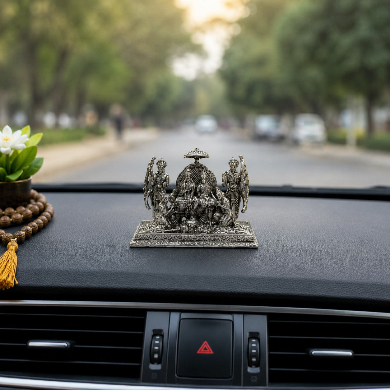 My Guru Ji silver finish brass Ram Darbar idol placed on a car dashboard with a mala and flower nearby.