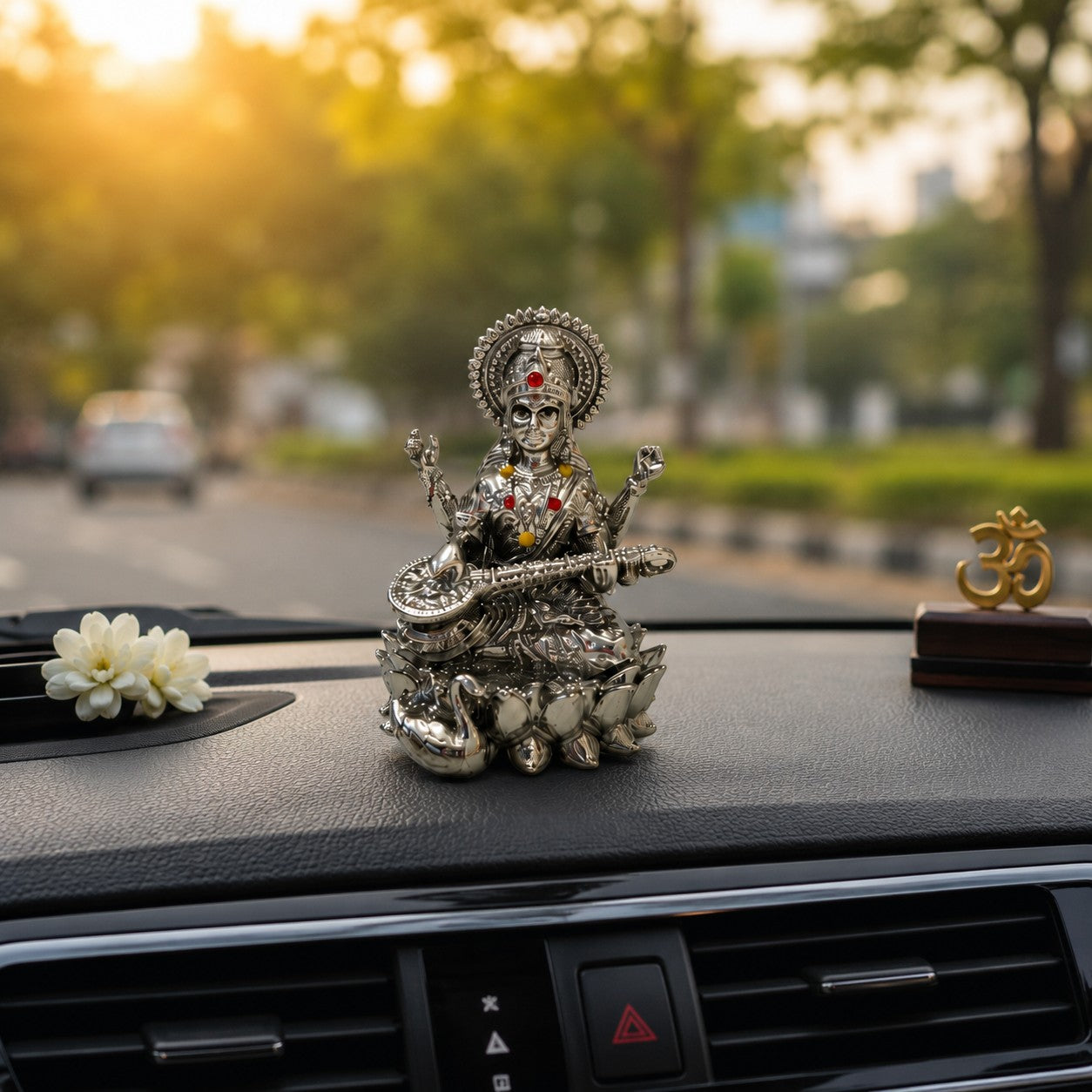 My Guru Ji silver finish brass Maa Saraswati idol with Veena, placed on a car dashboard with a small Om symbol.