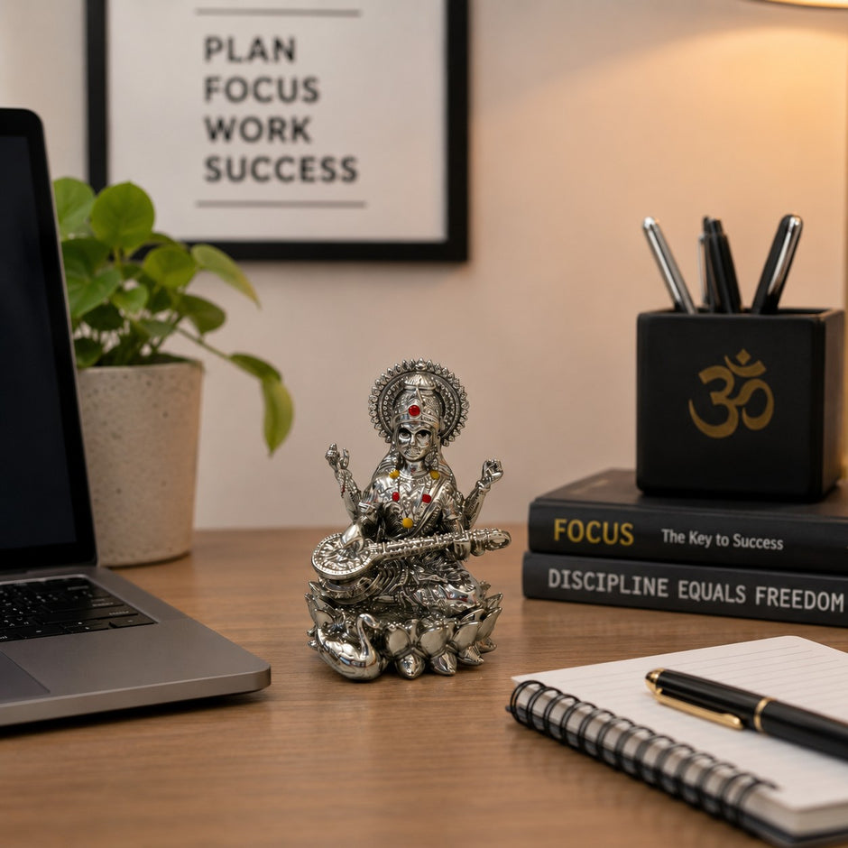My Guru Ji silver finish brass Maa Saraswati idol with Veena on a lotus, displayed on a desk with office stationery.