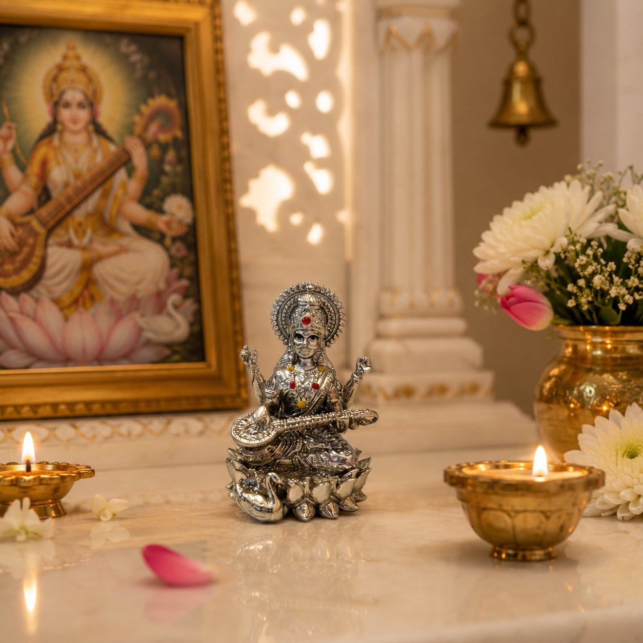 My Guru Ji silver finish brass Maa Saraswati idol seated on a lotus with a veena, displayed in a home temple setting.
