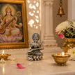 My Guru Ji silver finish brass Maa Saraswati idol seated on a lotus with a veena, displayed in a home temple setting.