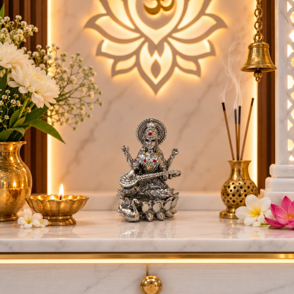 My Guru Ji silver finish brass Maa Saraswati idol seated on a lotus with a veena, displayed in a home temple setting.