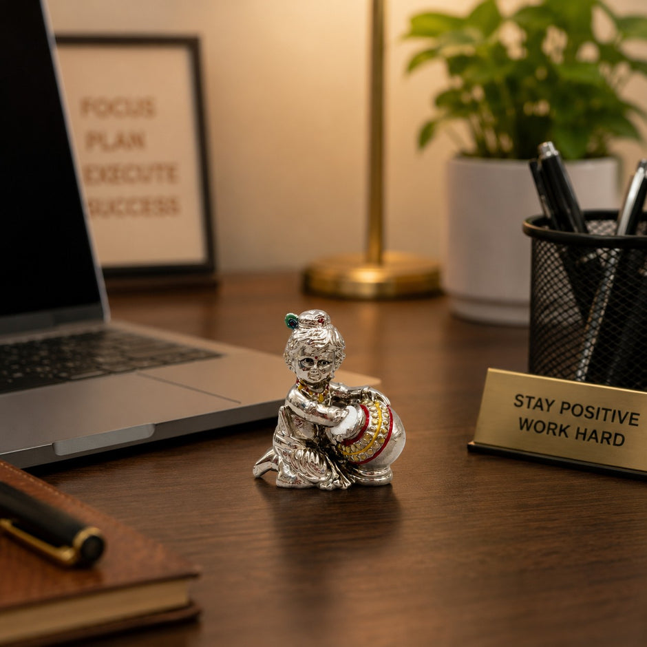 My Guru Ji silver finish brass Laddu Gopal Makhan Chor idol placed on an office desk with a laptop and stationery.