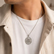 My Guru Ji round brass pendant with silver finish featuring an embossed portrait, worn by a man in a white shirt.