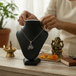 My Guru Ji silver plated brass Lord Ganesha pendant on a black display stand with a small Ganpati idol and diya.
