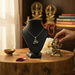 My Guru Ji silver plated brass Lord Ganesha pendant on a display stand next to a small Ganesha statue and diya.