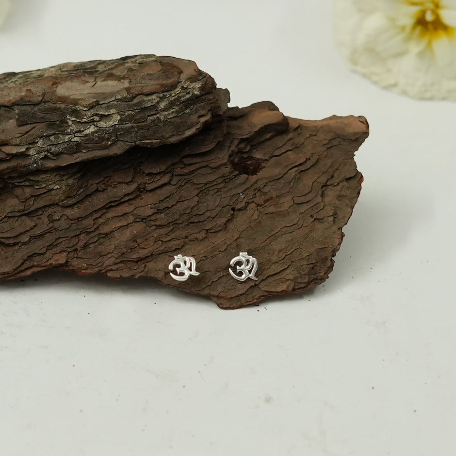My Guru Ji silver Om stud earrings featuring a polished finish on a rustic piece of tree bark