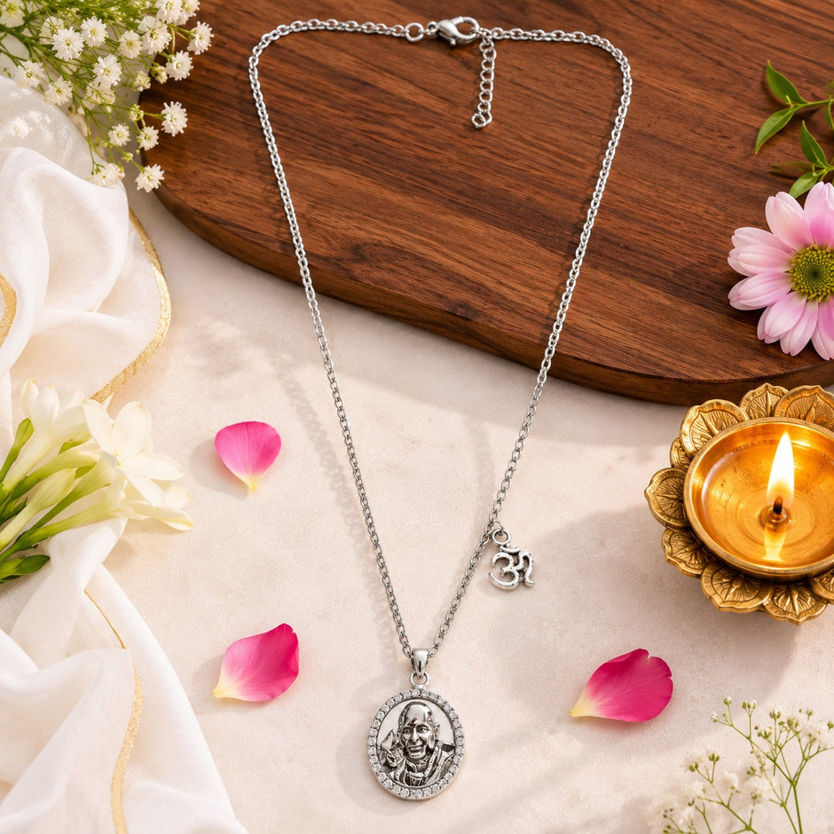My Guru Ji silver-finish brass pendant necklace featuring an OM charm, displayed with flowers and a lit diya lamp.
