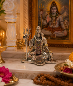My Guru Ji silver finish brass Lord Shiva idol in a meditative pose with a trishul, displayed on a home temple altar.