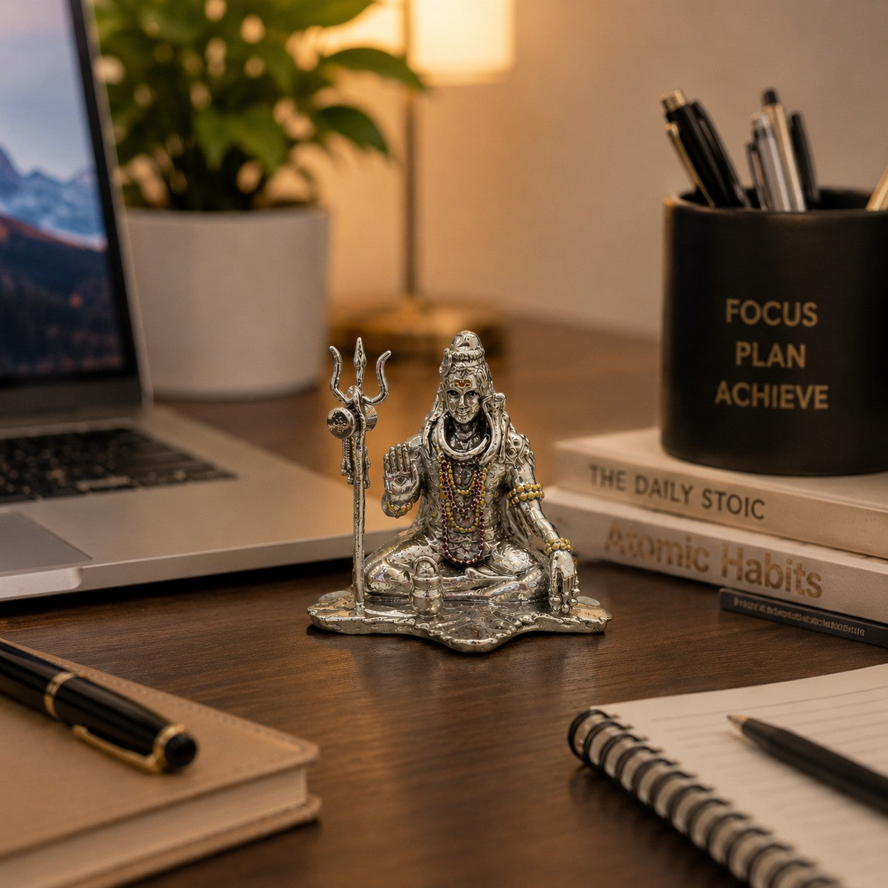 My Guru Ji silver finish brass Lord Shiva idol in meditative pose with Trishul on a desk near a laptop and books.