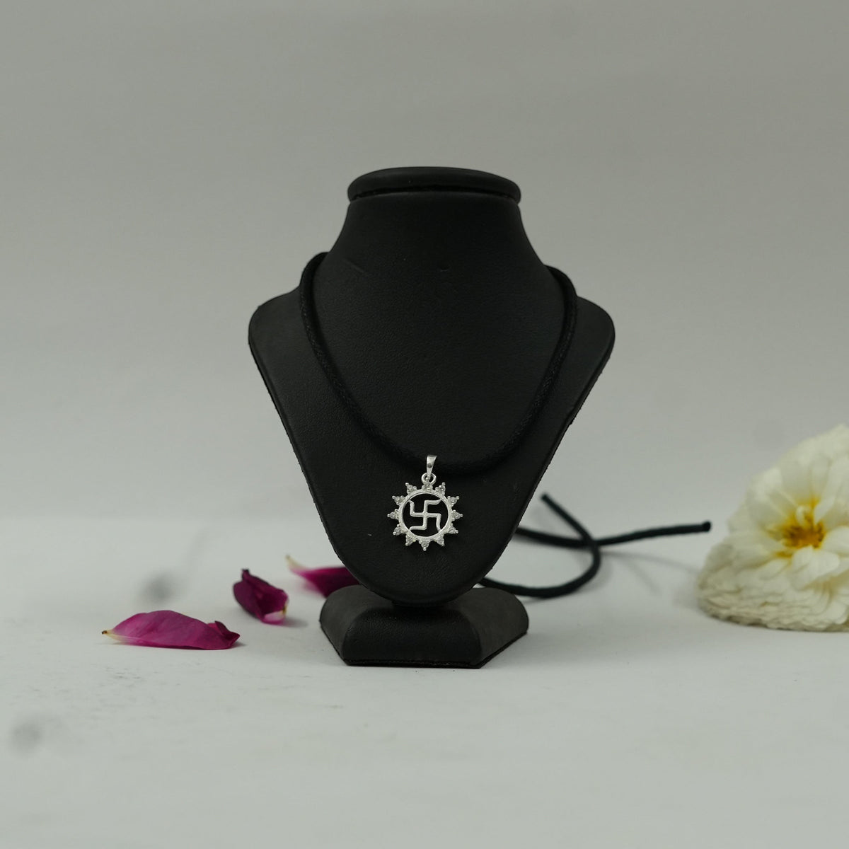 My Guru Ji silver finish Swastik pendant with vector chakra design on a black display stand with flower petals