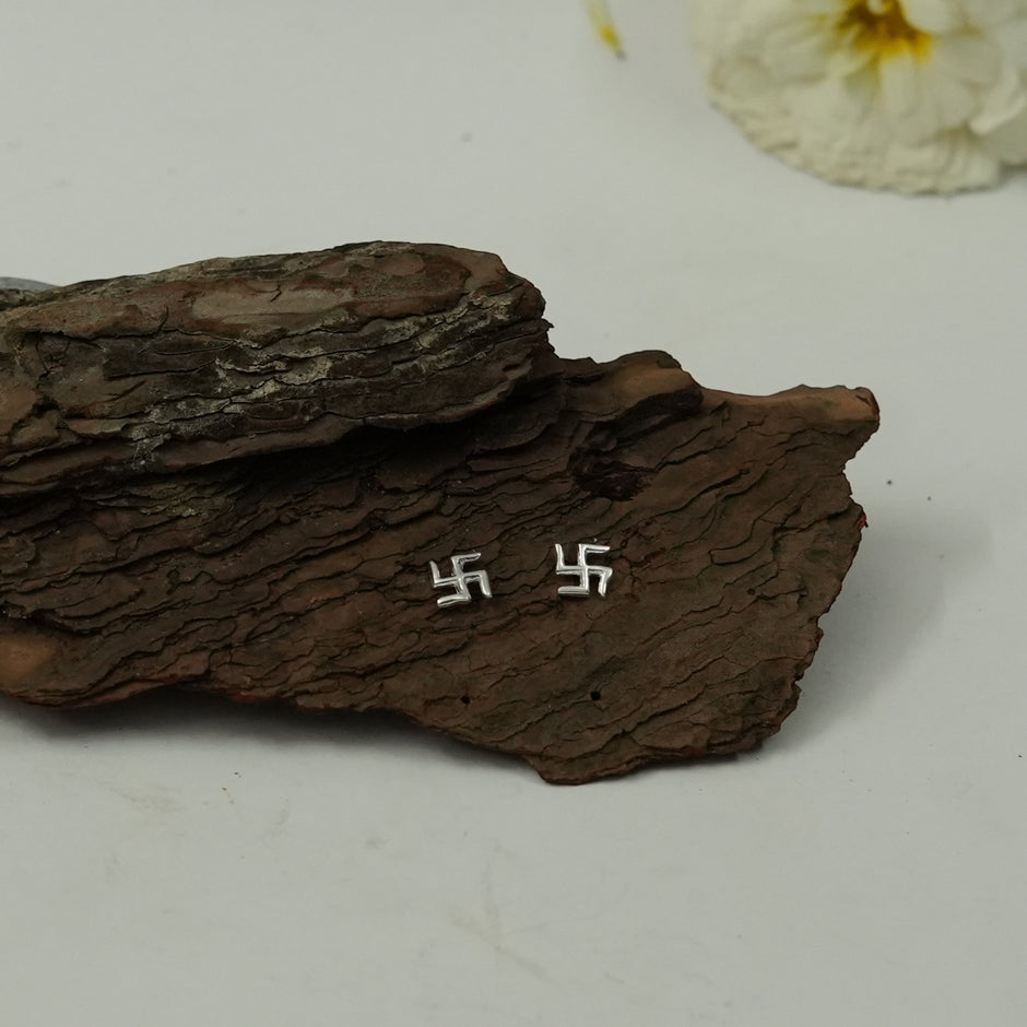My Guru Ji polished silver Swastik stud earrings featuring a minimal spiritual design on a rustic wood background.