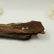 My Guru Ji polished silver Swastik stud earrings resting on a piece of natural wood for a spiritual aesthetic.